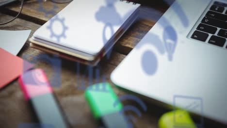 animación de múltiples iconos digitales contra el primer plano de equipos de oficina en una mesa de madera