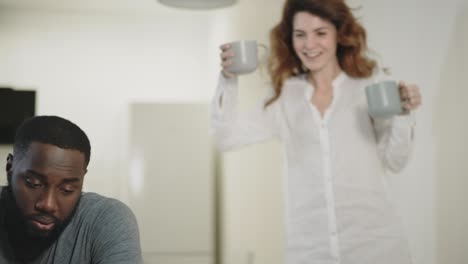 tired black man looking laptop screen at home. woman bringing tea to guy.