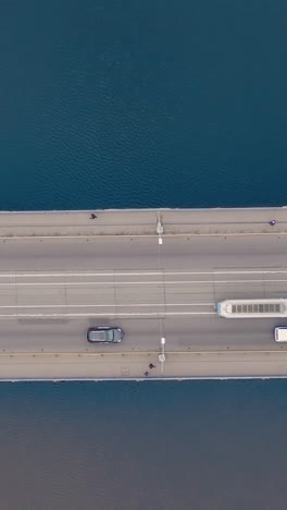 aerial shot bridge with tram, cars moving. drone flying over bridge with river, transport on a highway. vertical video