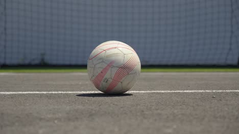 used soccer ball on asphalt field under bright sun near goal