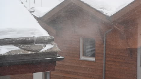 storm in a village, snow particles transported n’y the wind, a rooftop and gutter in the foreground, chalet, cabin behind