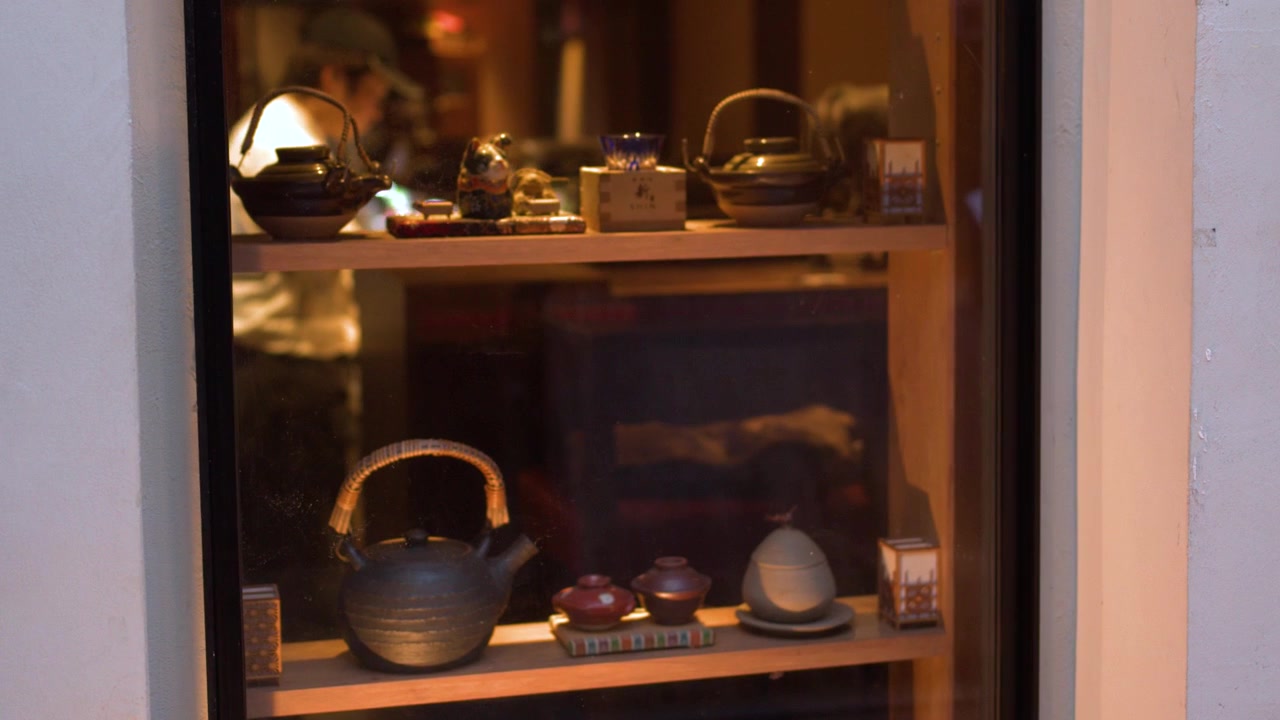 Static medium shot of handcrafted pottery on wooden shelves behind a glass window at night.