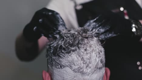 teñir el cabello de un joven por un peluquero profesional usando sus manos