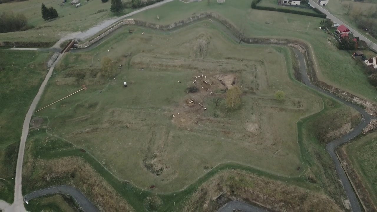An establishing aerial shot over Jablunkov Fortress reveals ancient settlement earthworks and defensive mounds illuminated by soft morning light.
