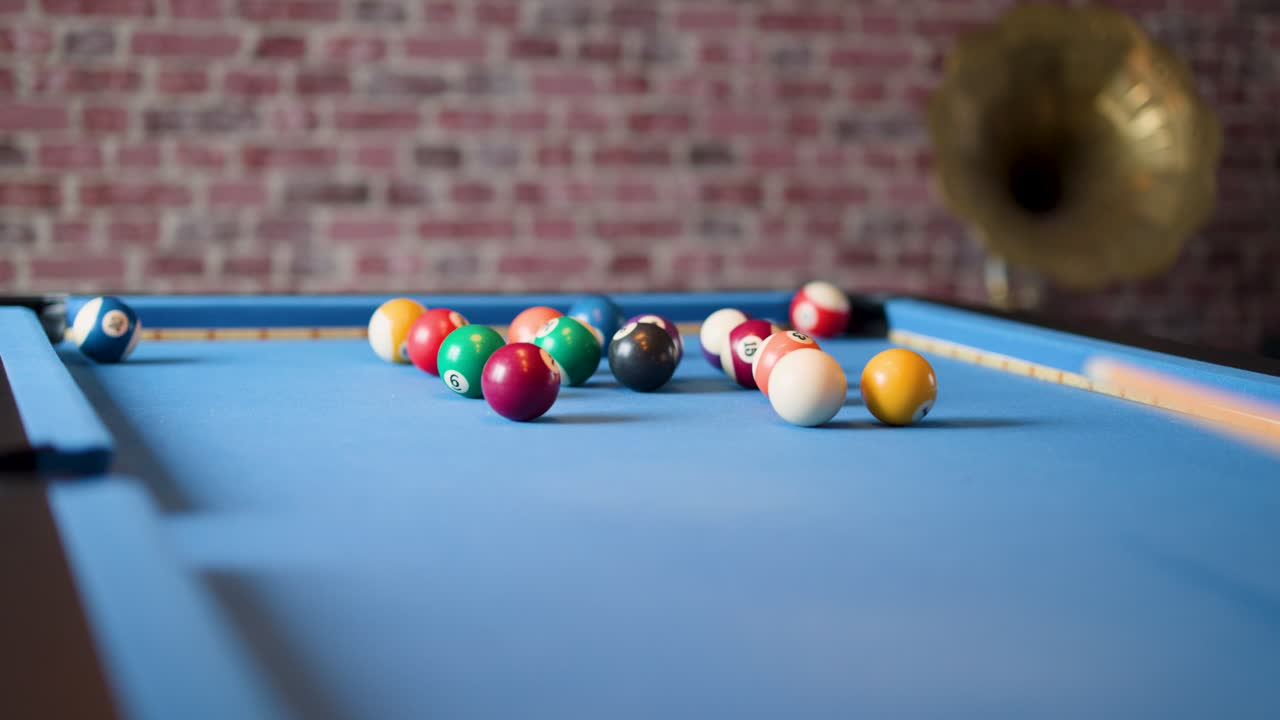 Billiard balls scatter rapidly across blue pool table, shallow depth of field, indoor ambient lighting