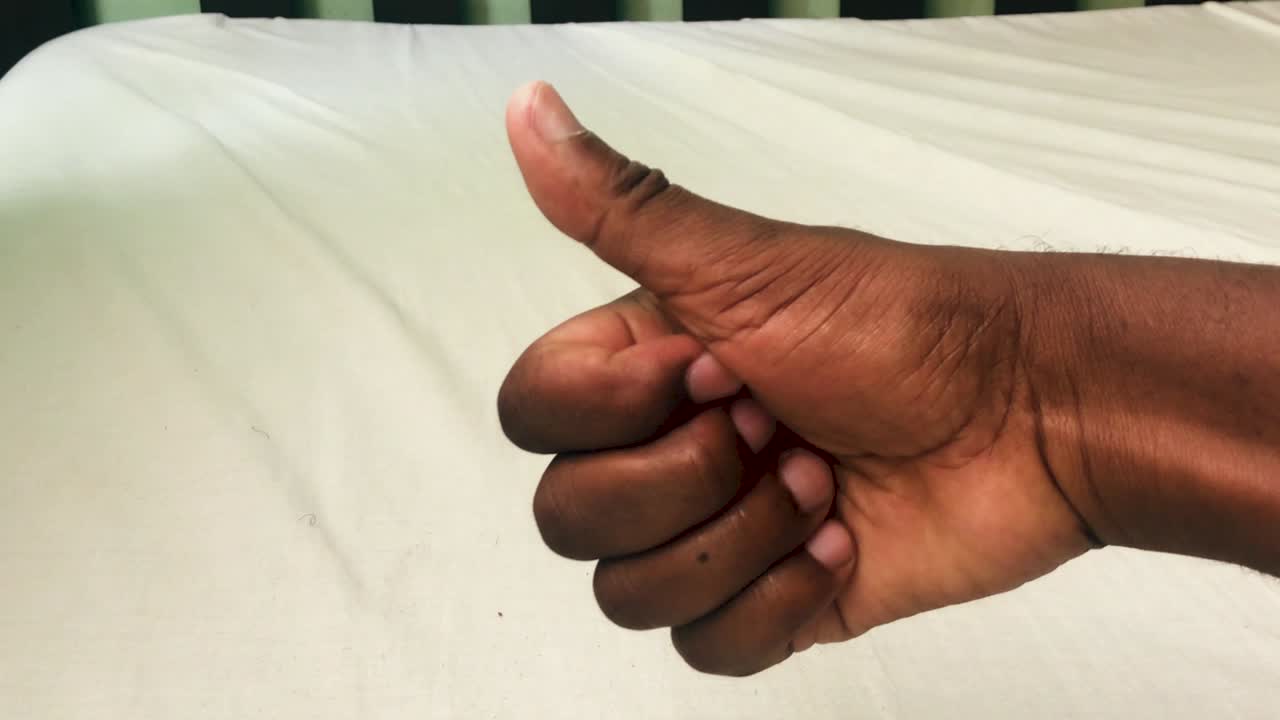 흰색 침대 커버가 있는 나무 침대 위에 있는 검은색 오른손의 엄지손가락