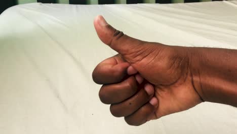 thumbs up of a black right hand over the wooden bed with white bedcover