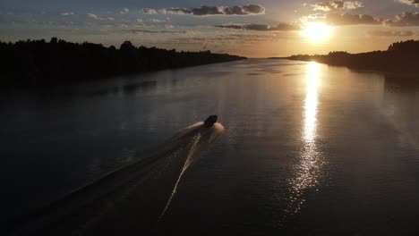 aerial following shot of small speedboat cruising on amazon river towards golden sunset in brazil