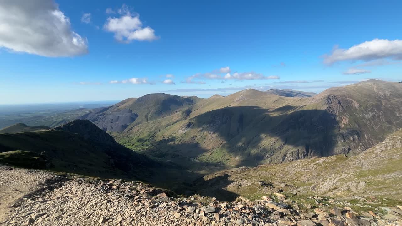 Rocky cliffs on Mount Snowdon under clear blue sky in Snowdonia National Park, showing peaceful mountain landscape with no people and soft sunlight on terrain.