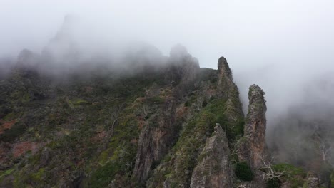 Drone-shot-of-Nuns-Valley-in-Madeira,-moving-forwards-towards-the-sharp-edge-of-the-ridge-with-thin-and-creepy-clouds-around