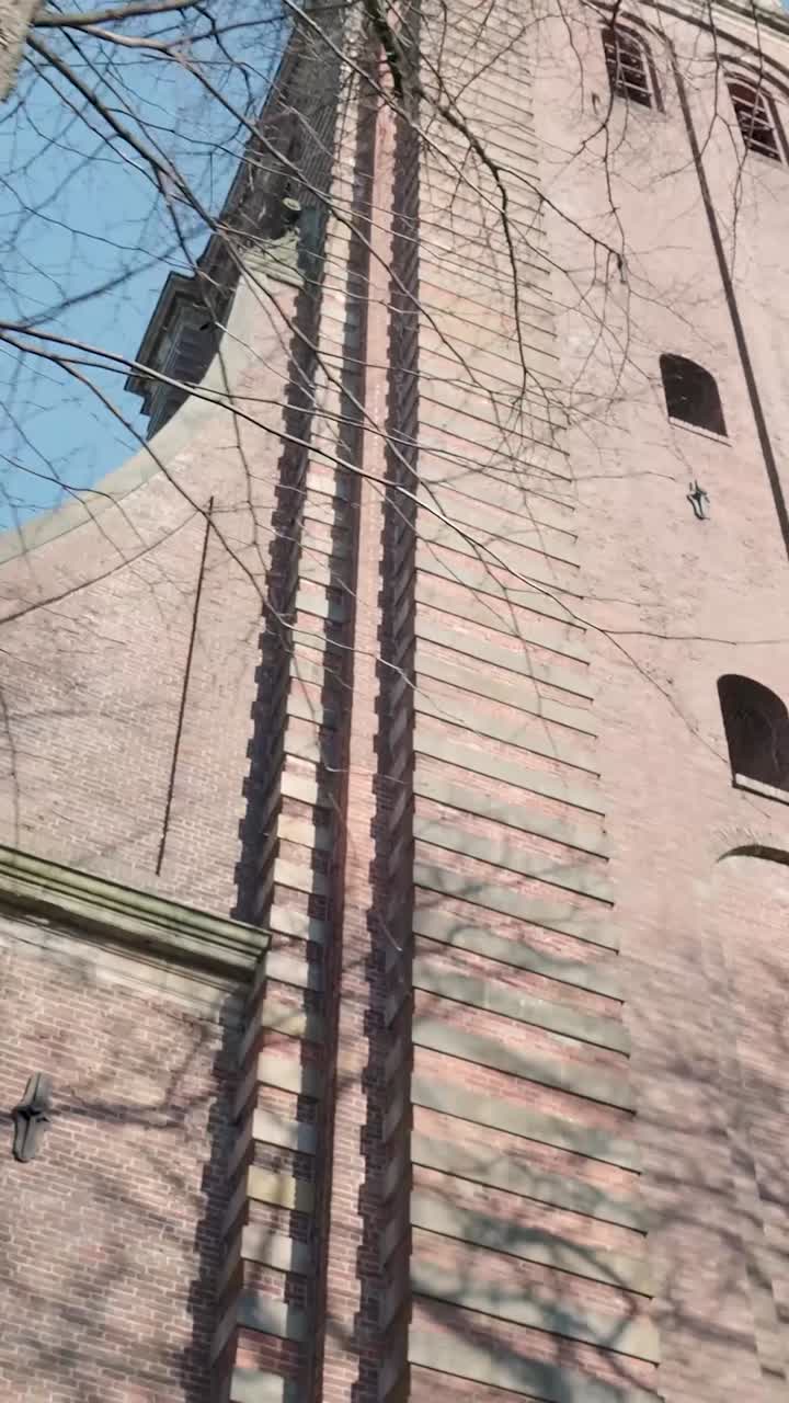 Torre de iglesia histórica de ladrillo con ramas de árboles desnudas contra el cielo azul