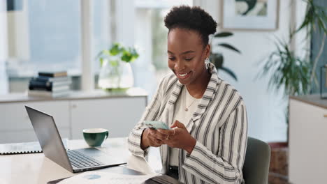 woman using smartphone while working on laptop in office