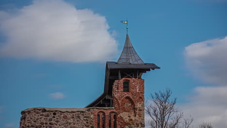 timelapse of the ruins of an ancient medieval castle in dobele, latvia during the daytime as clouds pass over, casting shadows onto the castle and spire