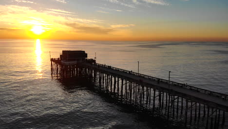 drone footage over newport beach pier with people in silhouette during a scenic southern california sunset over the ocean aerial