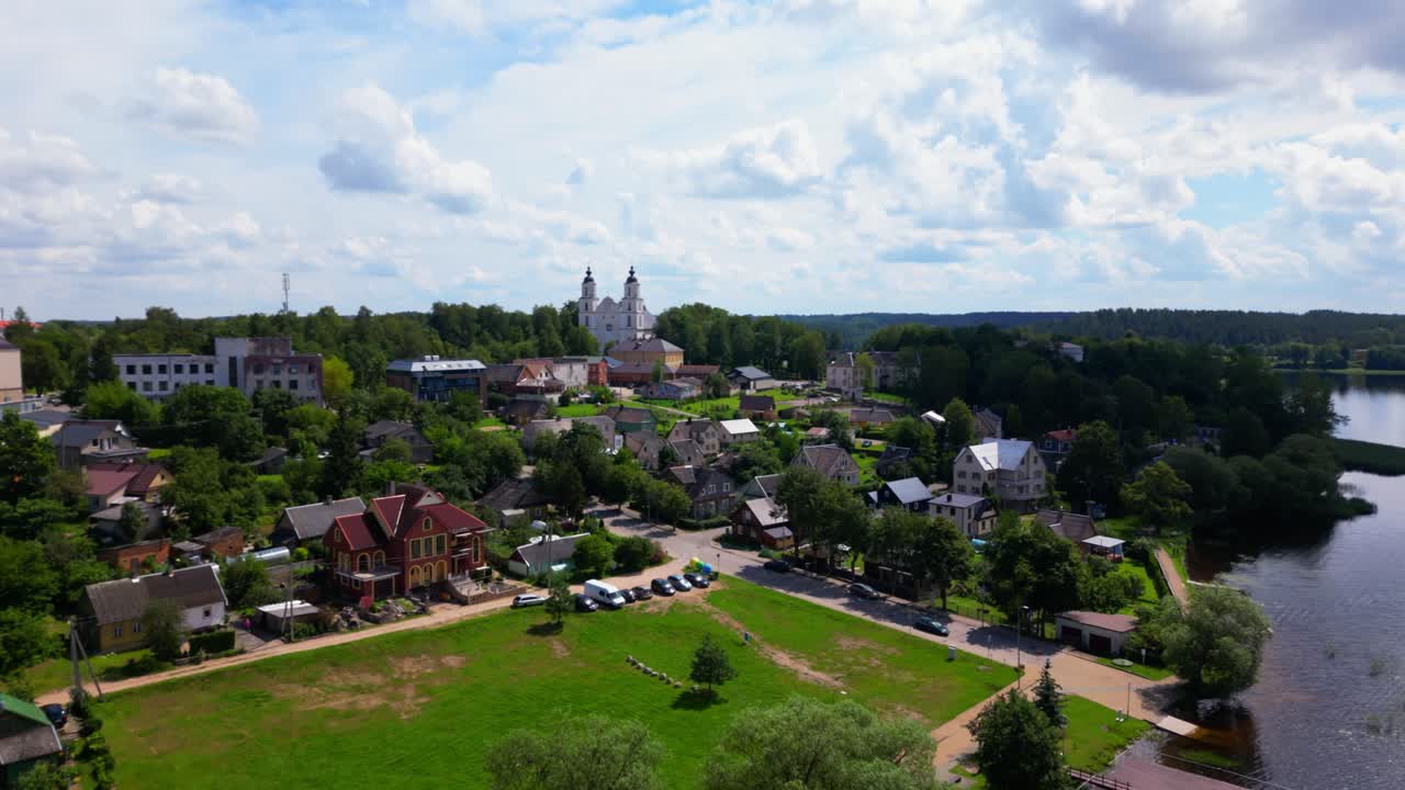 Wide angle aerial showing a lakeside town with central fountain and green slopes under a dynamic summer sky. Shot in Zarasai, Lithuania