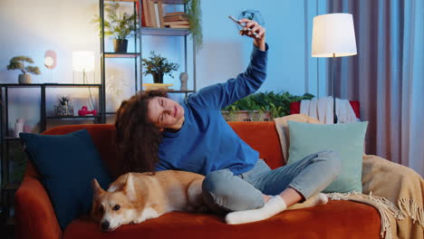 mujer amante de mascotas besando a un lindo perro corgi y tomando selfies a través de un teléfono inteligente en el sofá de la habitación de casa