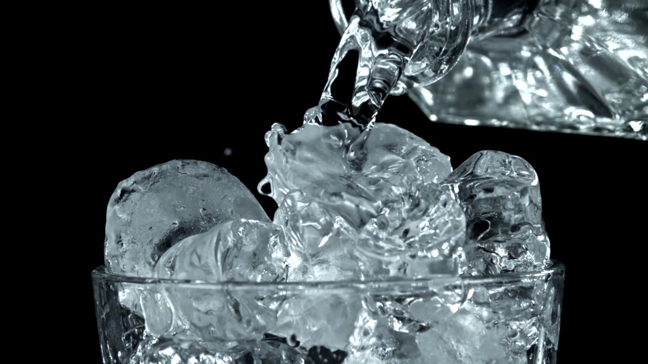 Versare acqua in un bicchiere con cubetti di ghiaccio, al rallentatore