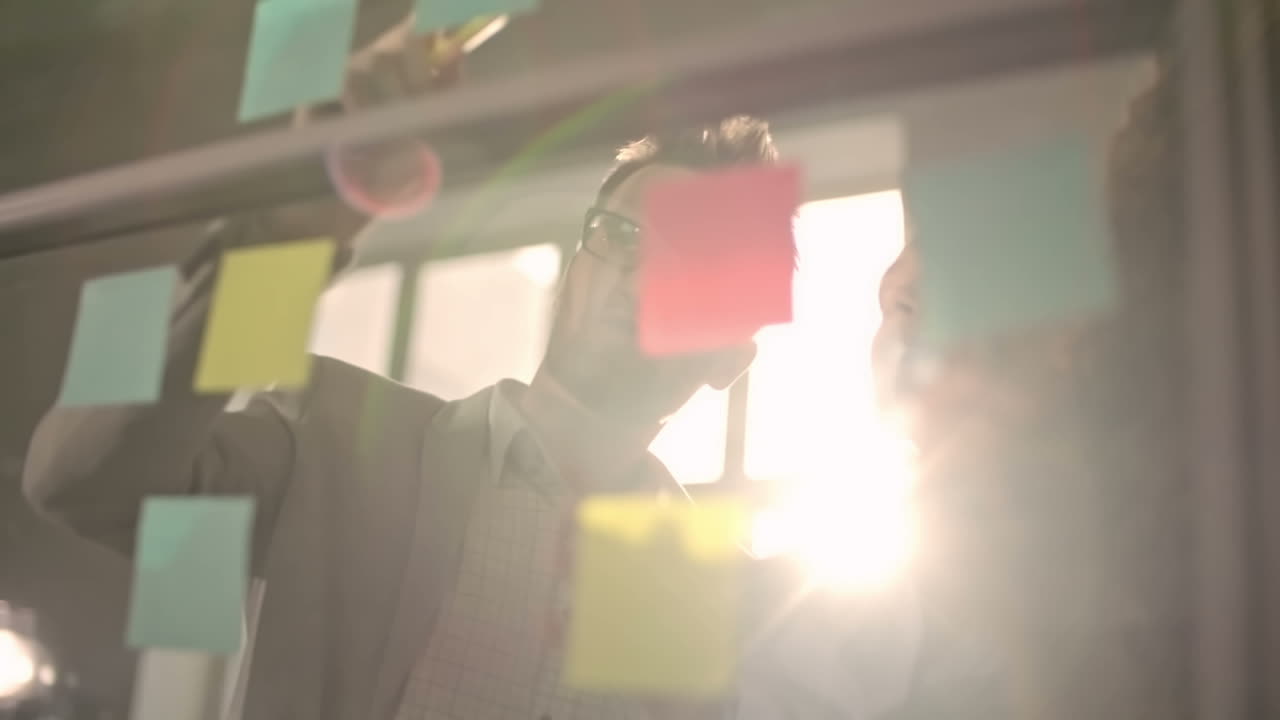 молодая бизнес-команда генерирует идеи и записывает их на клейких записках, прикрепленных к прозрачной стене