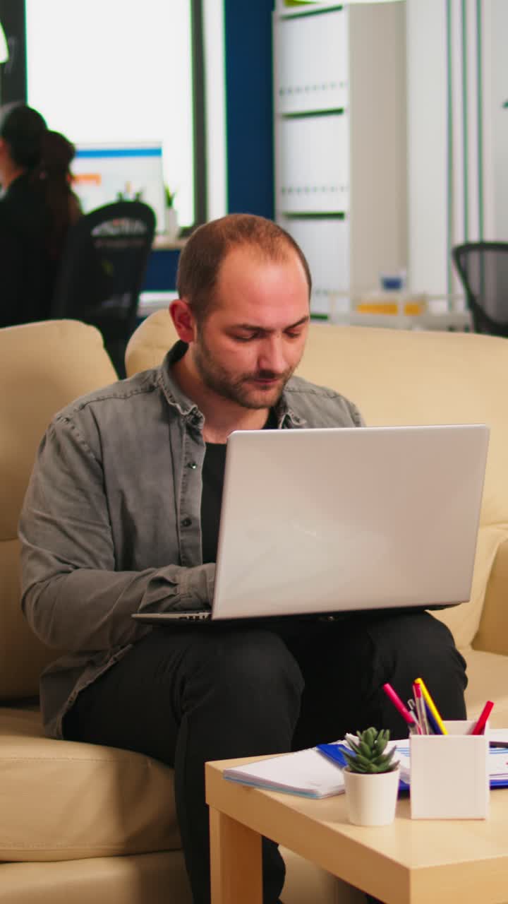 Vertical video Business man typing on laptop sitting on couch in start up office