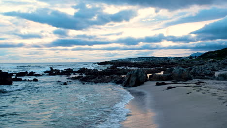 Paisaje-Nuboso-Escénico-Vibrante-De-La-Puesta-De-Sol-Mientras-Las-Olas-Golpean-La-Playa,-La-Muñeca-En