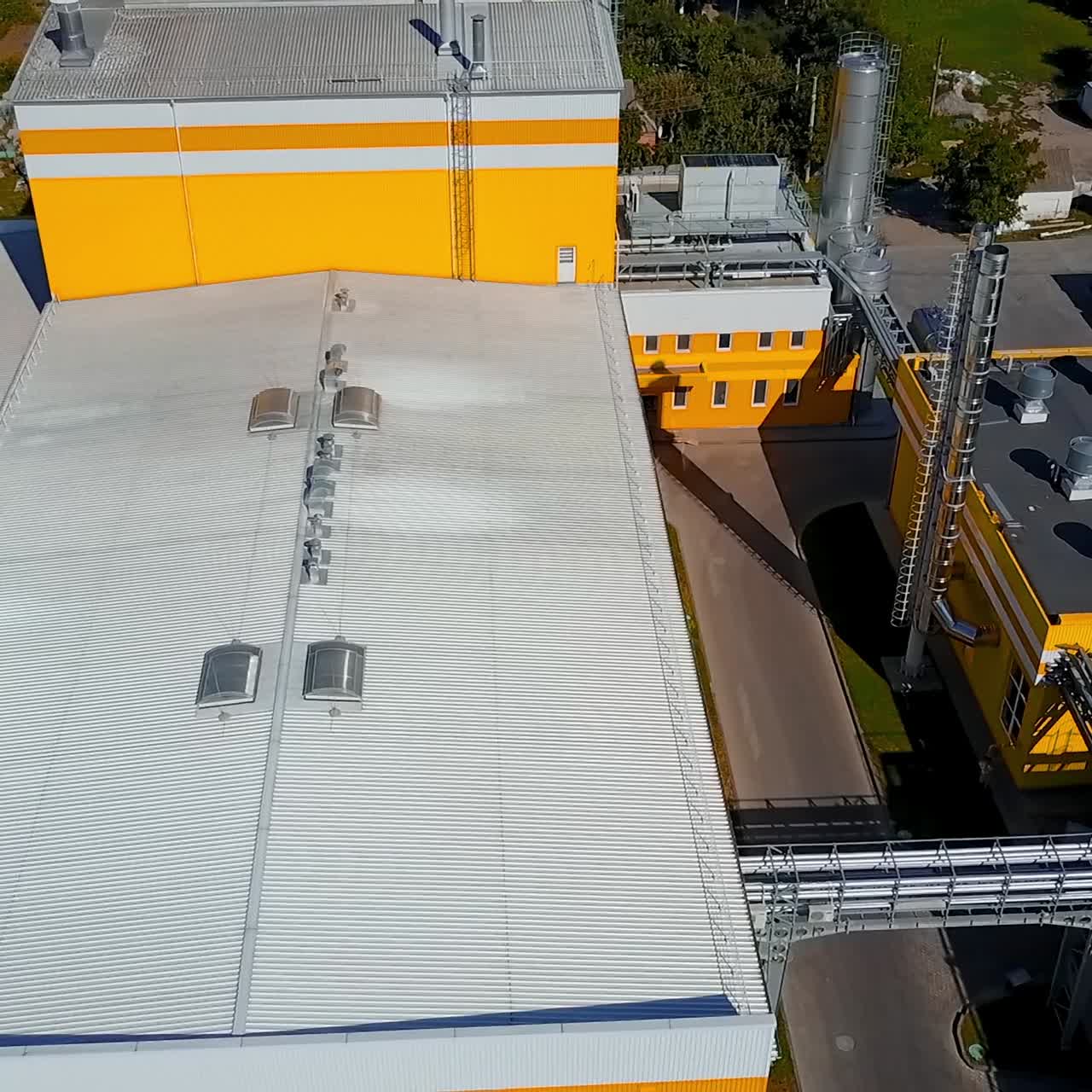 Yellow and white buildings of the industrial plant. Silver pipes among the premises of the factory. Circle drone footage