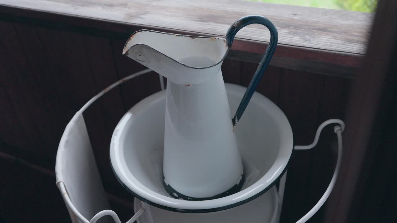 old enamel jug and basin set inside rustic washstand in soft indoor light