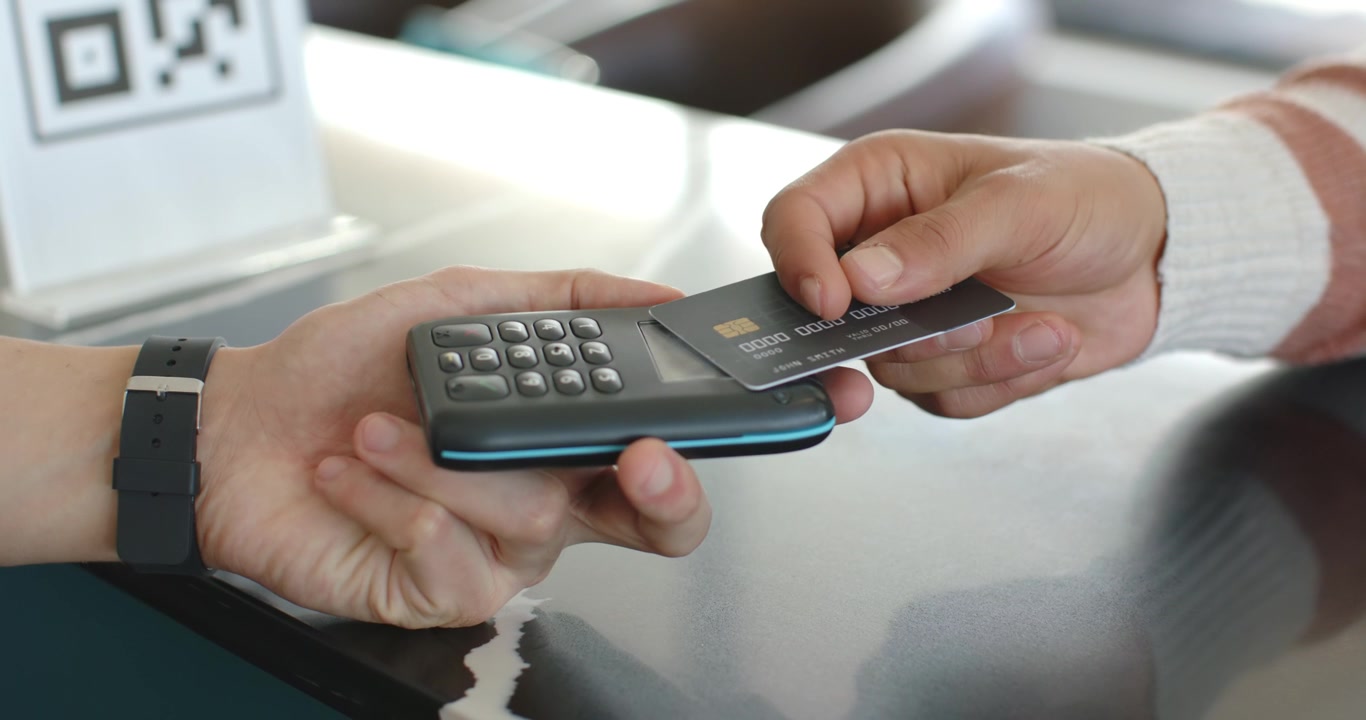 Due uomini, il commesso che tiene fermo il lettore mentre il cliente inserisce e sistema la carta con chip al bancone per pagare.