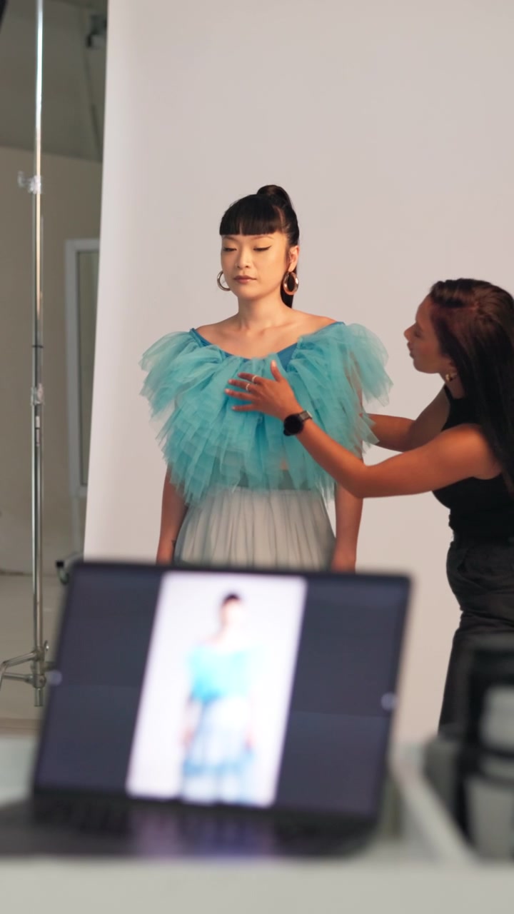 Stylista di moda che sistema un abito su una modella durante un servizio fotografico in studio