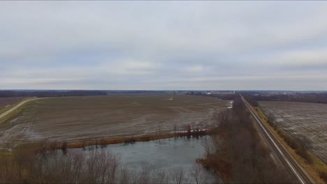automóviles, camiones y un autobús que viajan a través de un paso elevado que pasa sobre las vías del tren junto a un estanque en una carretera rural de illinois