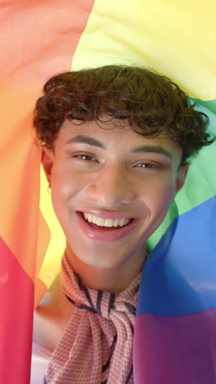 Vertical video: Smiling person wrapped in rainbow flag celebrating pride and diversity