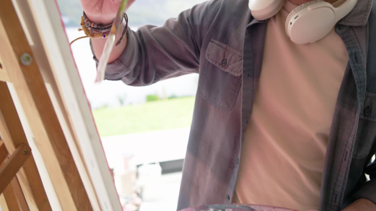 Un pennello si immerge in un barattolo di pittura bianca e si mescola sulla tavolozza, poi borda la tela vicino al balcone.