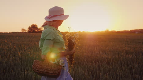 Frau-In-Einem-Hut-Mit-Einem-Strauß-Wilder-Blumen,-Die-Bei-Sonnenuntergang-Auf-Dem-Feld-Herumläuft-4k-Video
