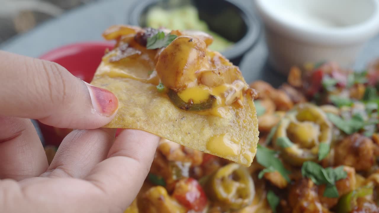 cerca de una mano sosteniendo un chip de nachos con queso, jalapeno y otros ingredientes