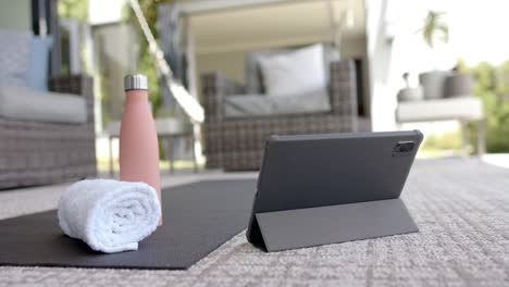 a tablet rests on yoga mat next to a water bottle and towel