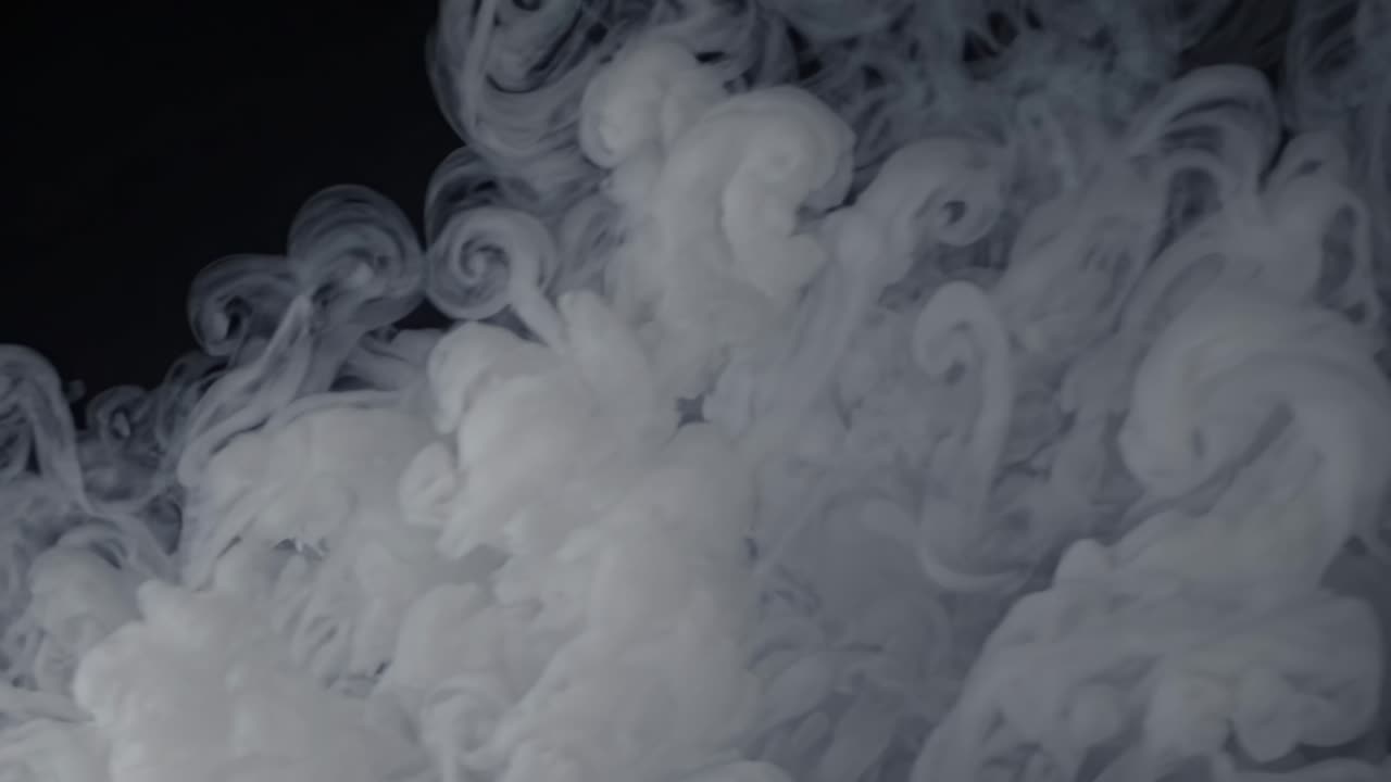 A mesmerizing video of swirling white smoke against a dark background, captured from a low-angle