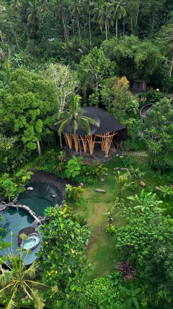 Drone captures a handcrafted bamboo villa mid-construction in Bali. Surrounded by forest edge and lush growth, it highlights eco-friendly craftsmanship and tropical architecture in progress
