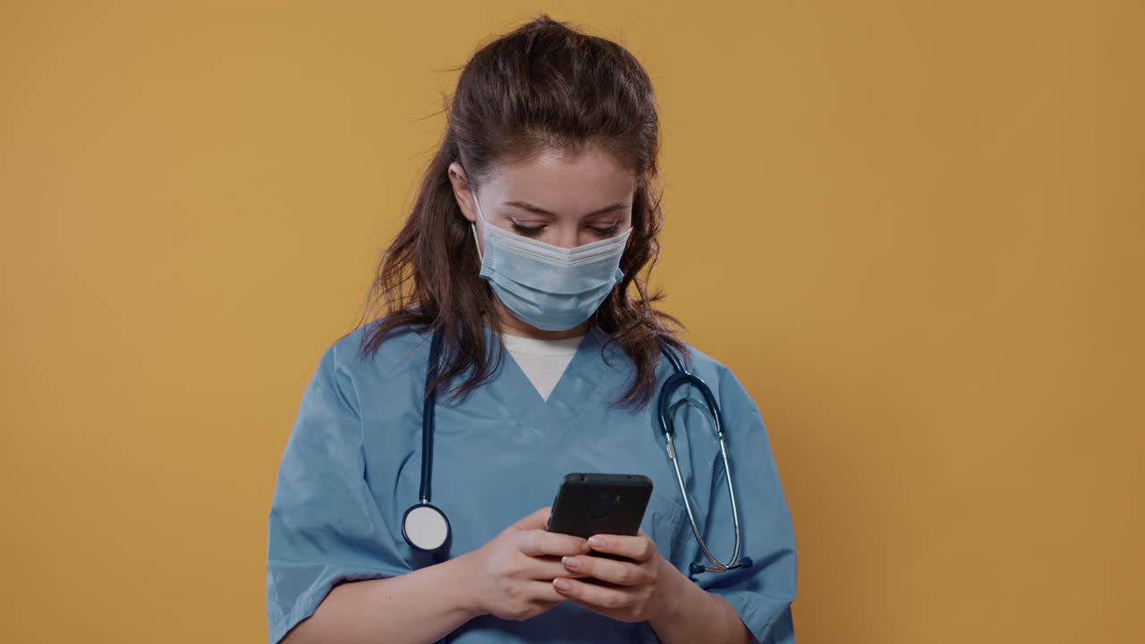 Retrato de un médico con uniforme de hospital y mascarilla quirúrgica que sostiene un smartphone y escribe un mensaje, mostrando un mockup de pantalla verde
