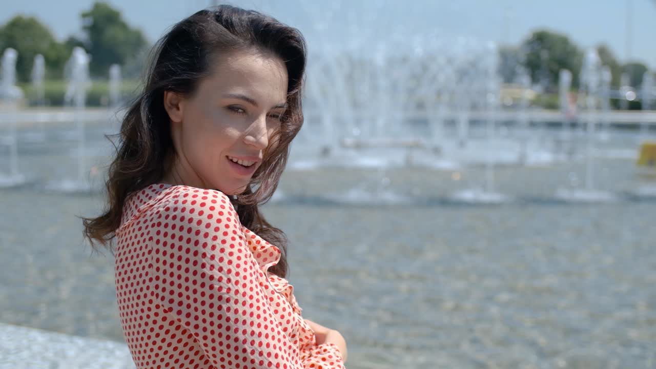 Ritratto di bella ragazza in abiti estivi colorati seduta vicino a una fontana