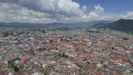 Drone-aerial-footage-of-urban-central-american-colonial-city-Quetzaltenango-Xela,-Guatemala-with-colorful-rooftops-and-cityscape-close-to-mountains