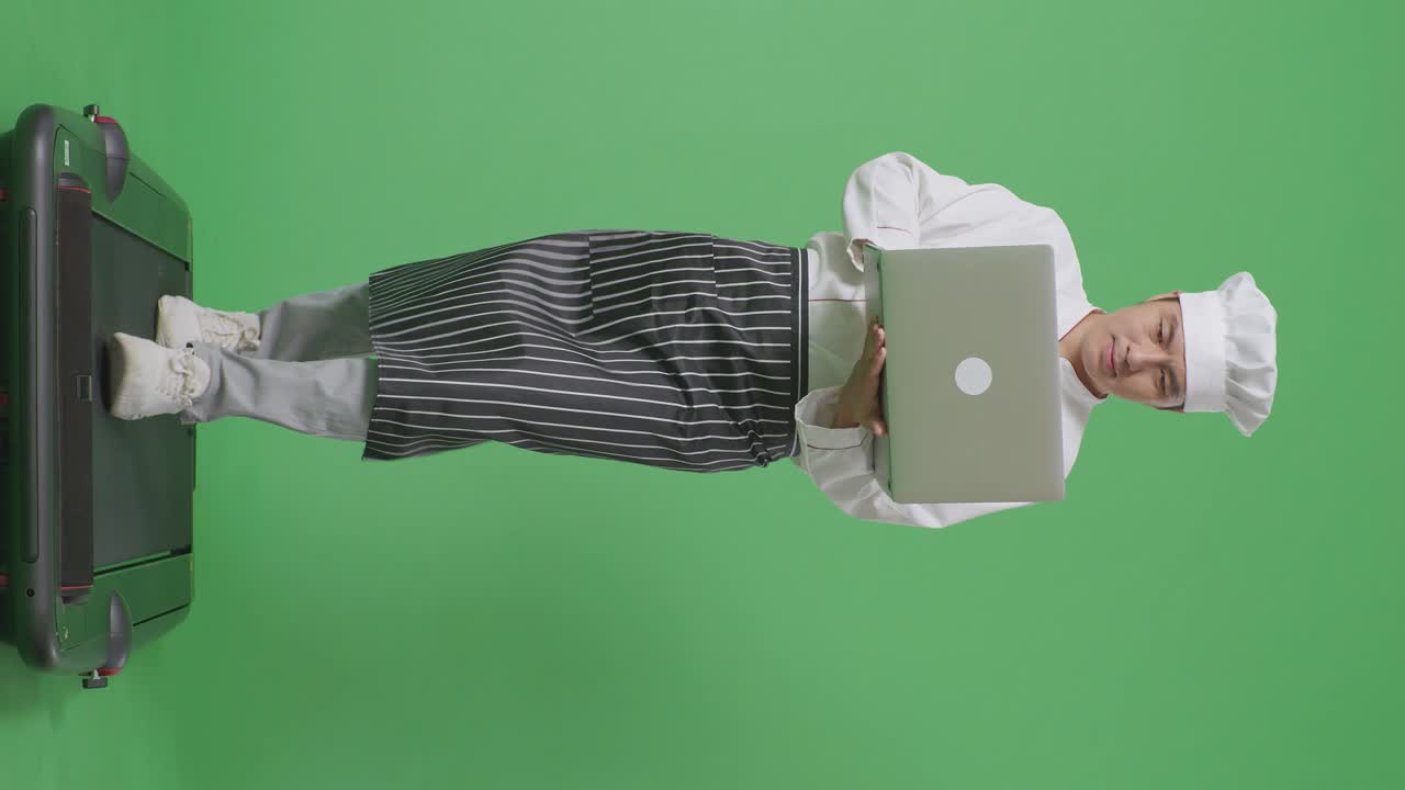 cuerpo lleno de cocinero hombre asiático usando una computadora portátil mientras caminaba en la cinta de correr en el estudio de fondo de pantalla verde