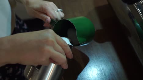 slowmo - professional female barista stirs the milk and pours to other frothing jug