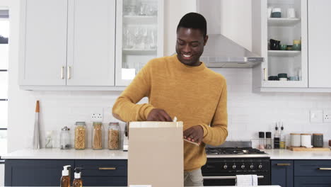smiling man opening package in kitchen, enjoying holiday gift unboxing