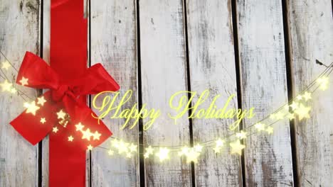 Animation-of-text,-happy-holidays,-in-yellow,-over-string-lights-and-red-bow-on-wood-boards