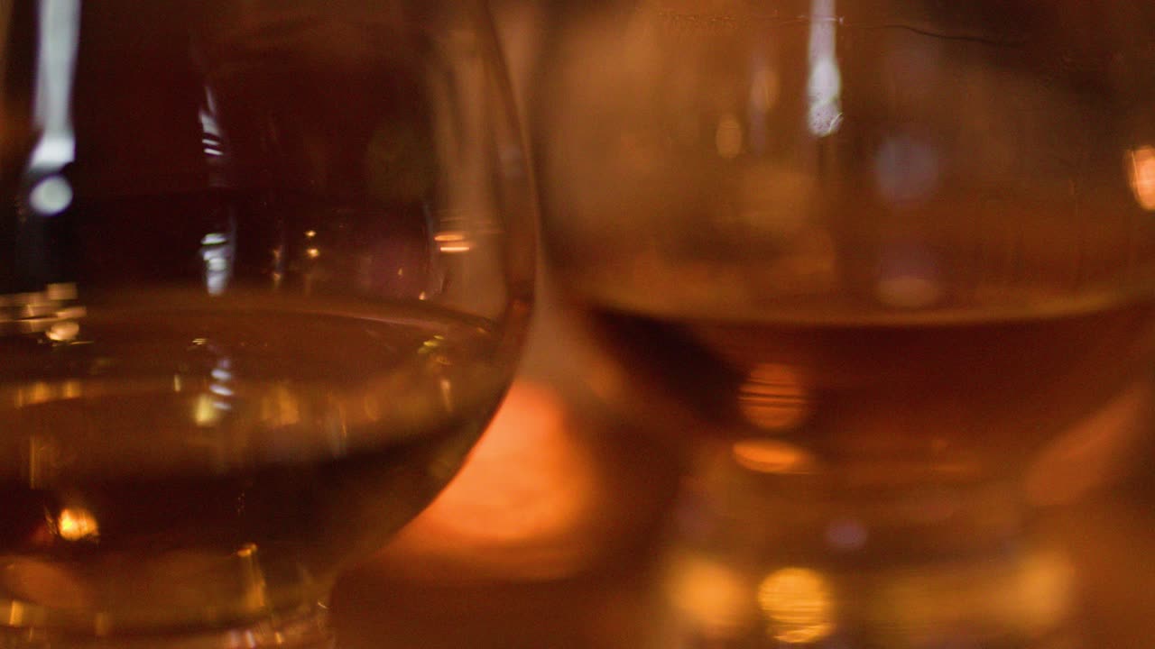 Liquido ambrato che si agita all'interno di un bicchiere di cristallo sotto una luce calda e soffusa con sfondo bokeh