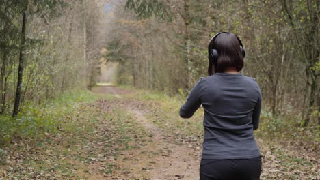 La-Mujer-Se-Pone-Los-Auriculares,-Activa-Su-Aplicación-De-Fitness-En-El-Reloj-Inteligente-Y-Empieza-A-Correr-Por-El-Bosque---Vista-Trasera-Americana