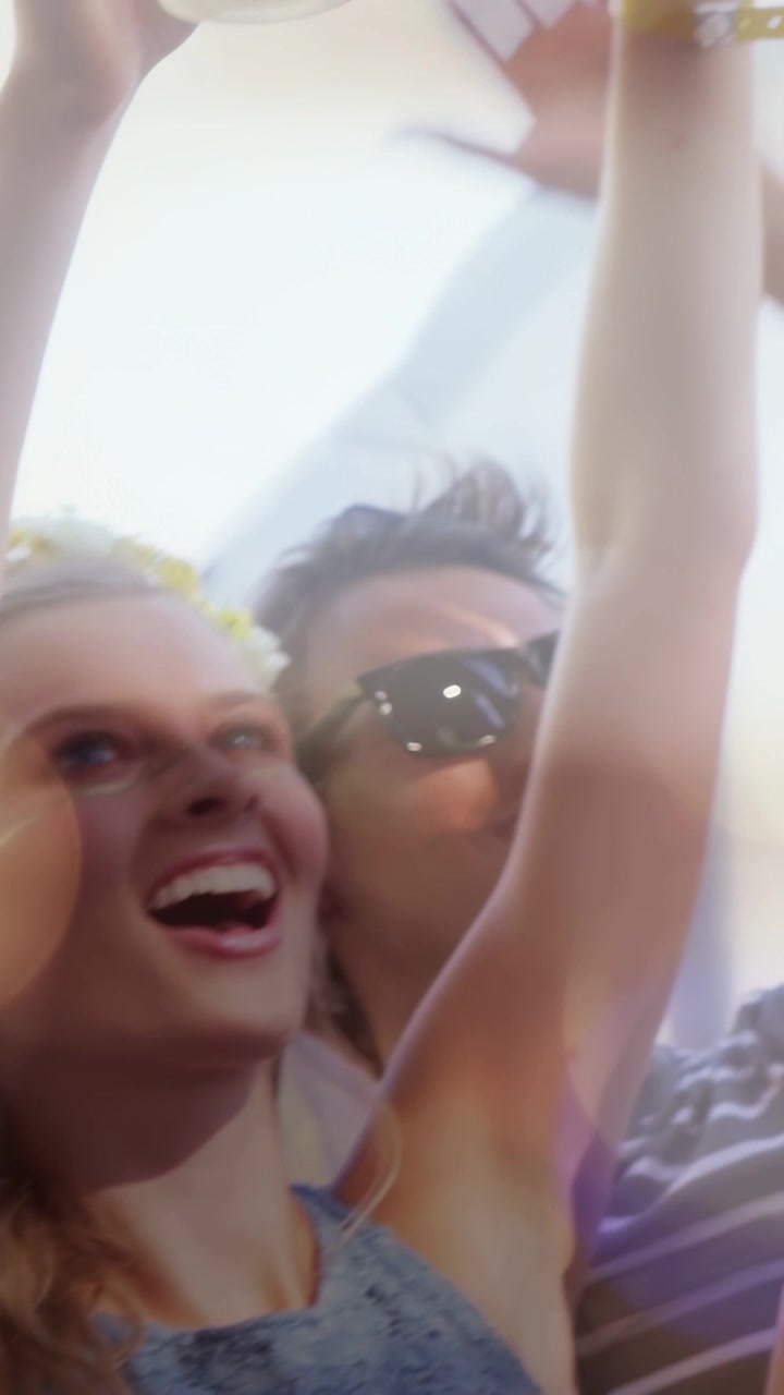 Video verticale: Donna che alza il braccio mentre festeggia, un gruppo che si allunga per prendere un bicchiere trasparente a un festival musicale.