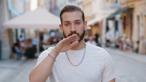 a man with a beard standing on a street in a city, making a gesture with his hand.