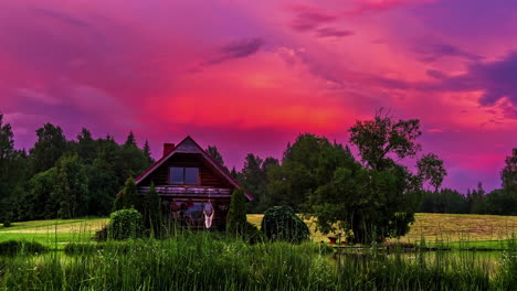 un video de lapso de tiempo de una cabaña rural sola en un prado con nubes rosadas dinámicas que se mueven vívidamente en el fondo