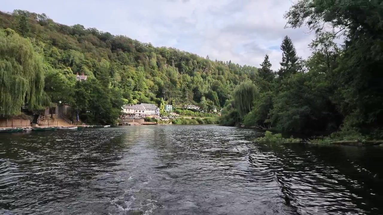 Scia di una barca che increspa il fiume Wye mentre le case lungo la riva di Symonds Yat si trovano sotto colline boscose