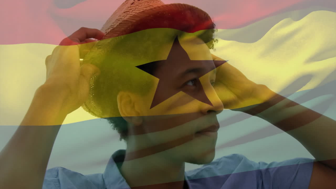 Adjusting straw hat with Ghana flag overlay, person standing outdoors smiling